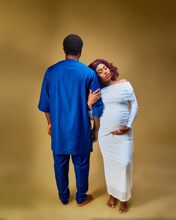 A serene maternity portrait featuring a couple in a studio with a golden backdrop.